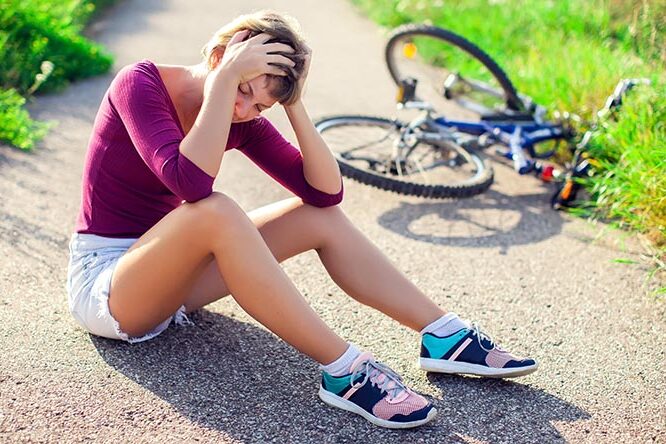 Frau mit kurzen Haaren sitzt auf dem Boden mit einen Fahrrad im Hintergrund